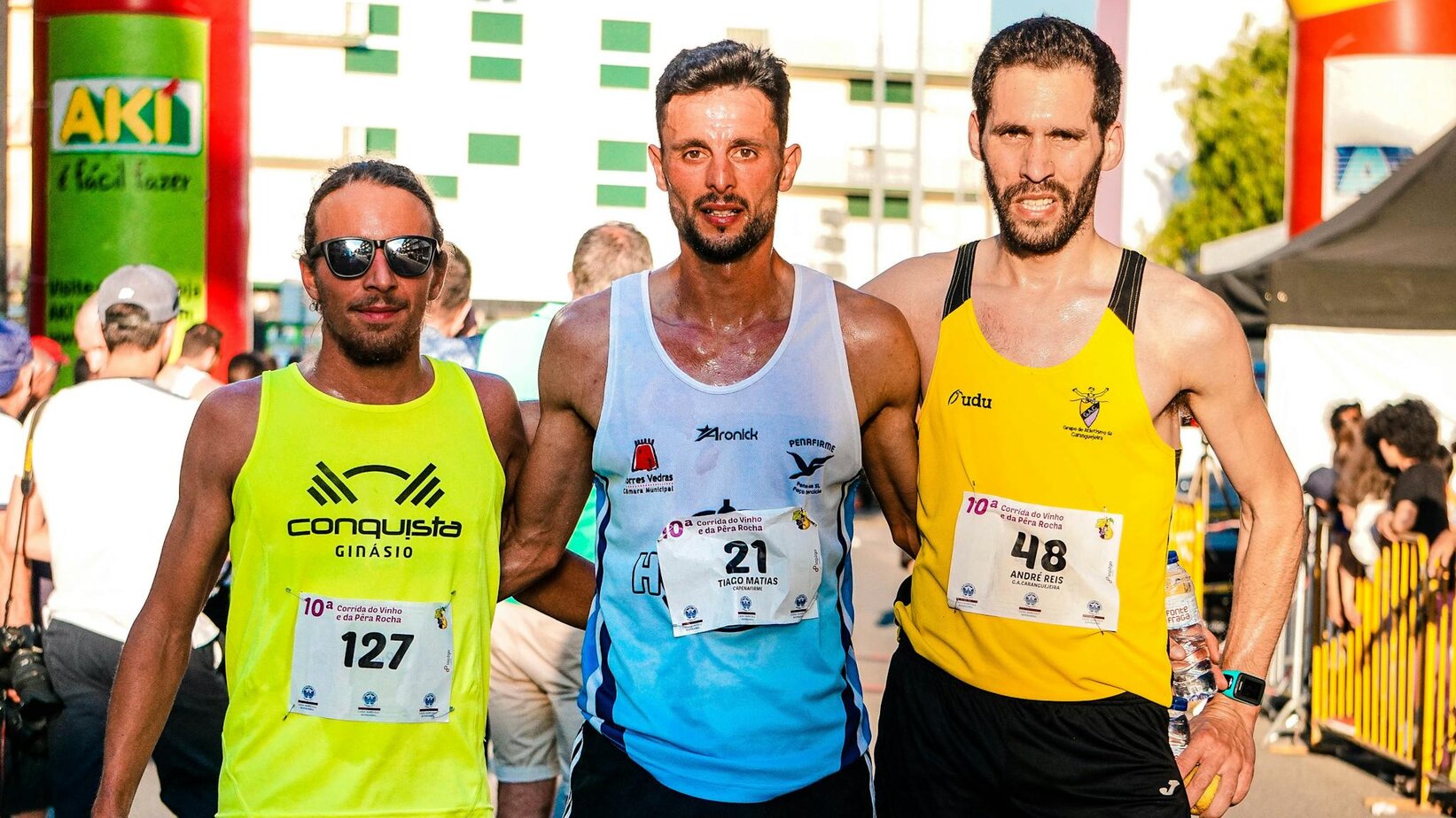 Three male marathon runners posing together in bright daylight after a race event outdoors.